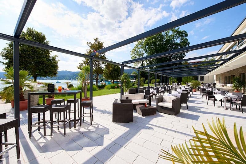 Palmenterrasse im Parkhotel Poertschach mit Sessel und Stuehle und Blick auf den Woerthersee