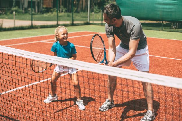 Tennislehrer trainiert mit Kind auf Tennisplatz