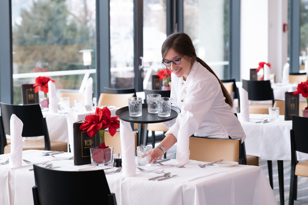 Mitarbeiterin im Service steht im Hotelrestaurant und deckt den Tisch auf.