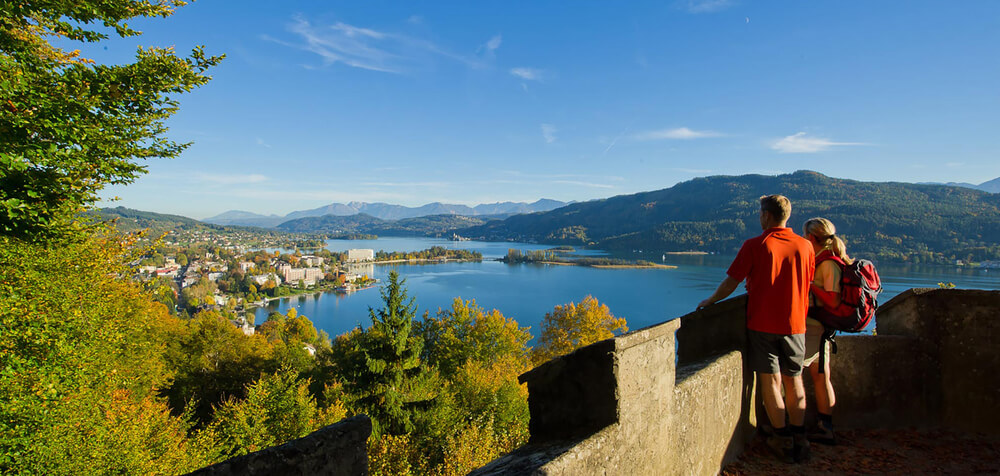 Ein Paar steht auf der hohe Gloriette und im Hintergrund und blickt auf die Halbinsel im Woerthersee runter