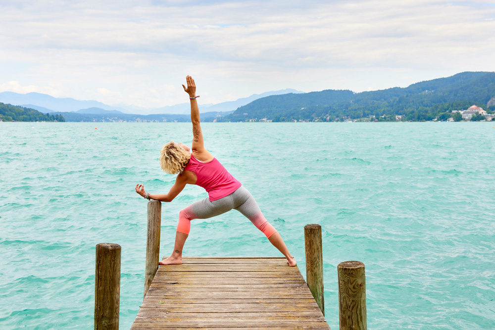 Frau steht am Steg und macht Yoga