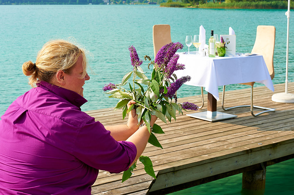 Frau steht am Badestrand des Parkhotel Pörtschach und bindet Blumen zusammen. Im Hintergrund ist ein gedeckter Tisch