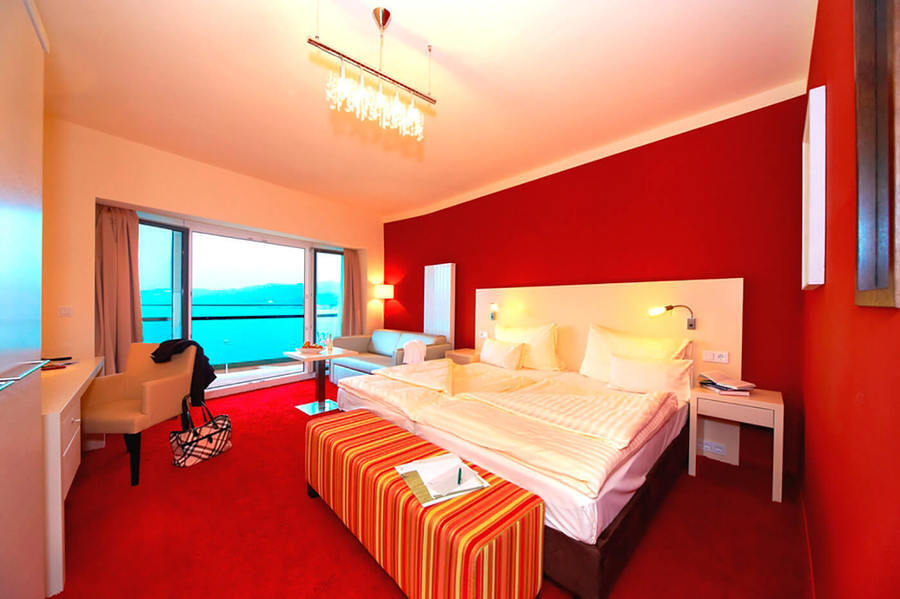 Rotes Zimmer mit Bett, Sessel und Balkon mit Seeblick