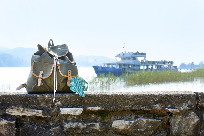 Rucksack auf der Mauer und Schiff im Hintergrund am Woerthersee 
